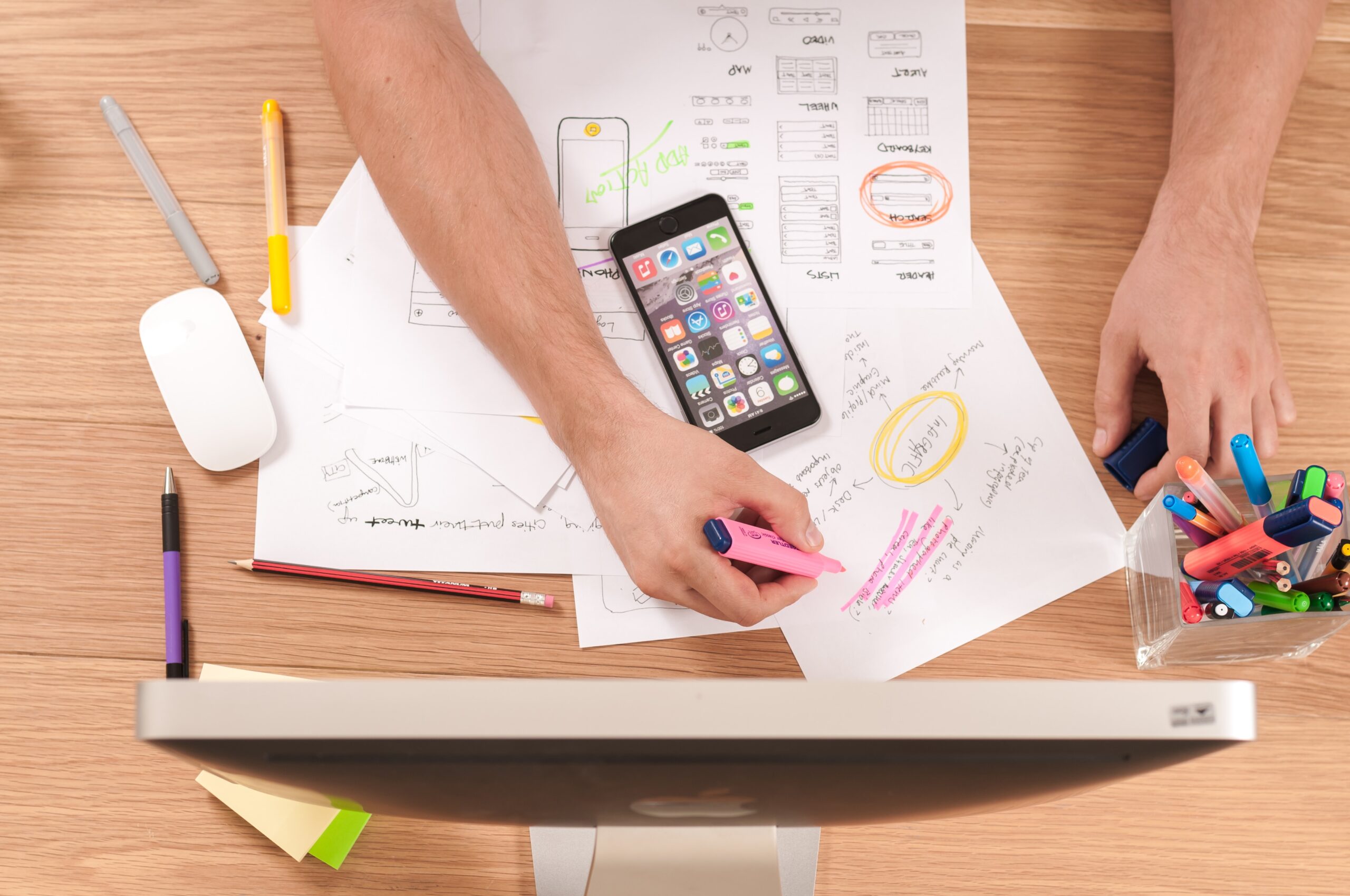 A desk with a screen, smartphone, notes, drawings and lots of colourful pens. Photo: Firmbee.com/Unsplash.